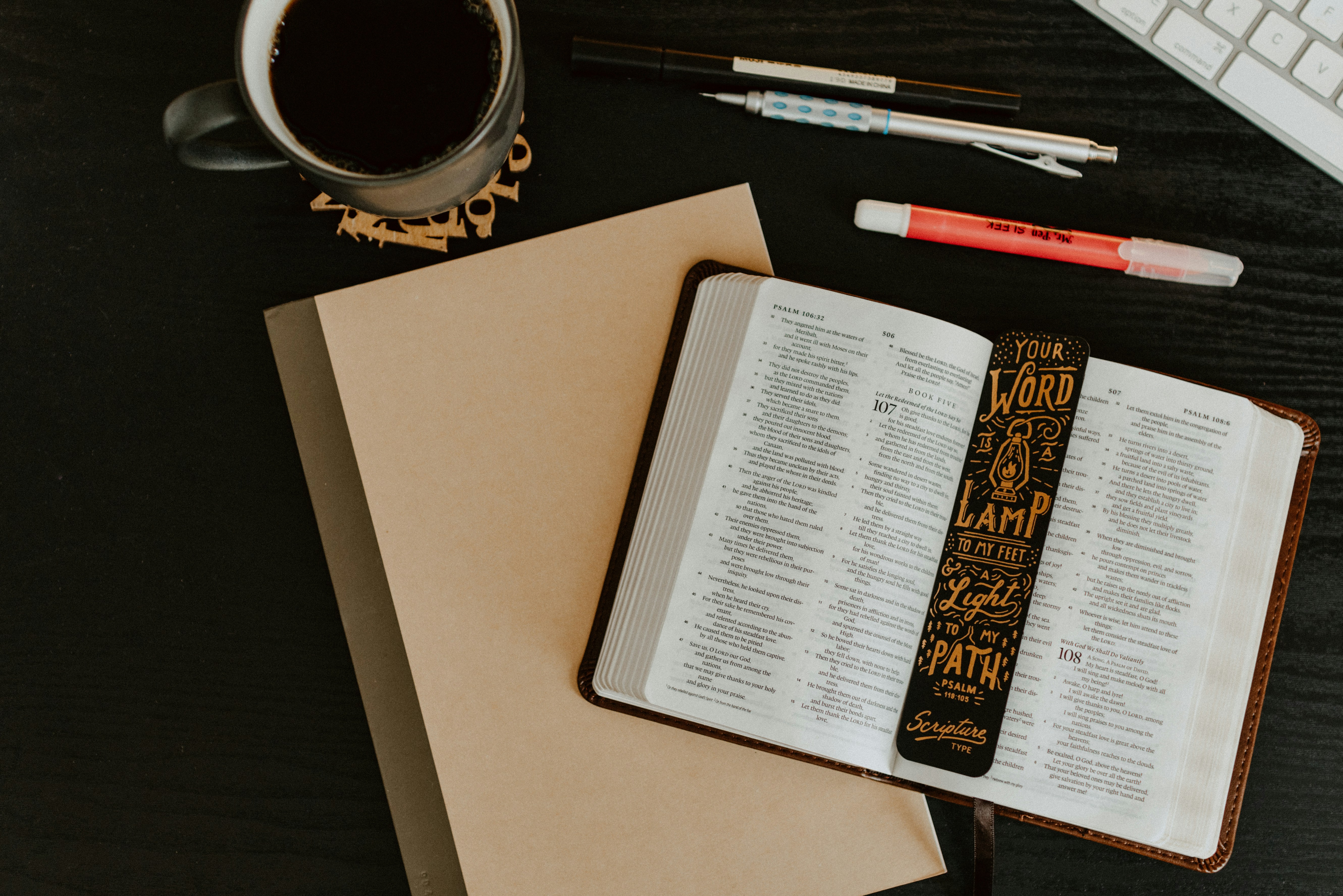 Open Bible with journal, coffee, and pens on a desk during quiet time